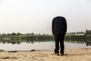 A man stands with his head down in front a river