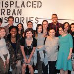 A class poses in front of the words "Displaced Urban Histories" spray painted onto gallery wall