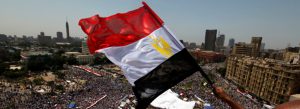 A man holds the Egyptian flag over a crowd in Tahrir Square during the Egyptian revolution of 2011