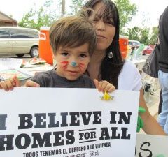 Little boy holding a sign saying "I Believe in Homes for All"