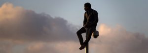 photo of a man sitting on top of a lamp post