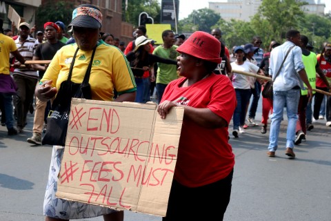 Two women protest holding "#EndOutsourcing #FeesMustFall" sign