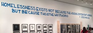 Martha Rosler's exhibit wall with the quote "Homelessness exists not because the housing system is not working but because this is the way it works - Peter Marcuse"