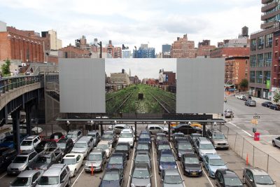 A billboard of train tracks overgrown with greenery installed over a parking lot
