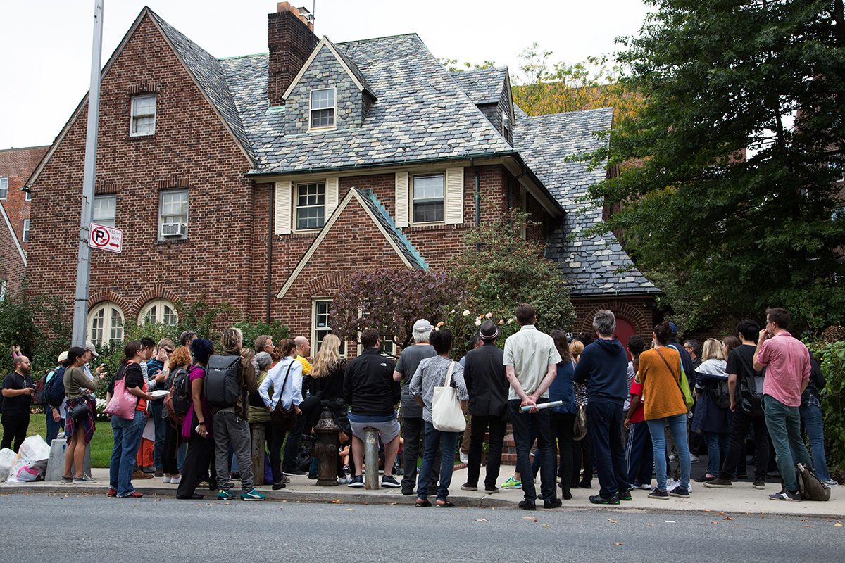 A large crowd of people stand in front of a residential house
